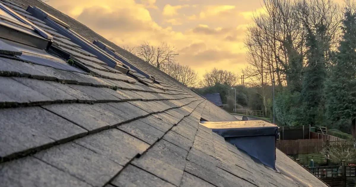 A shingled roof in need of replacement with the sun setting behind it